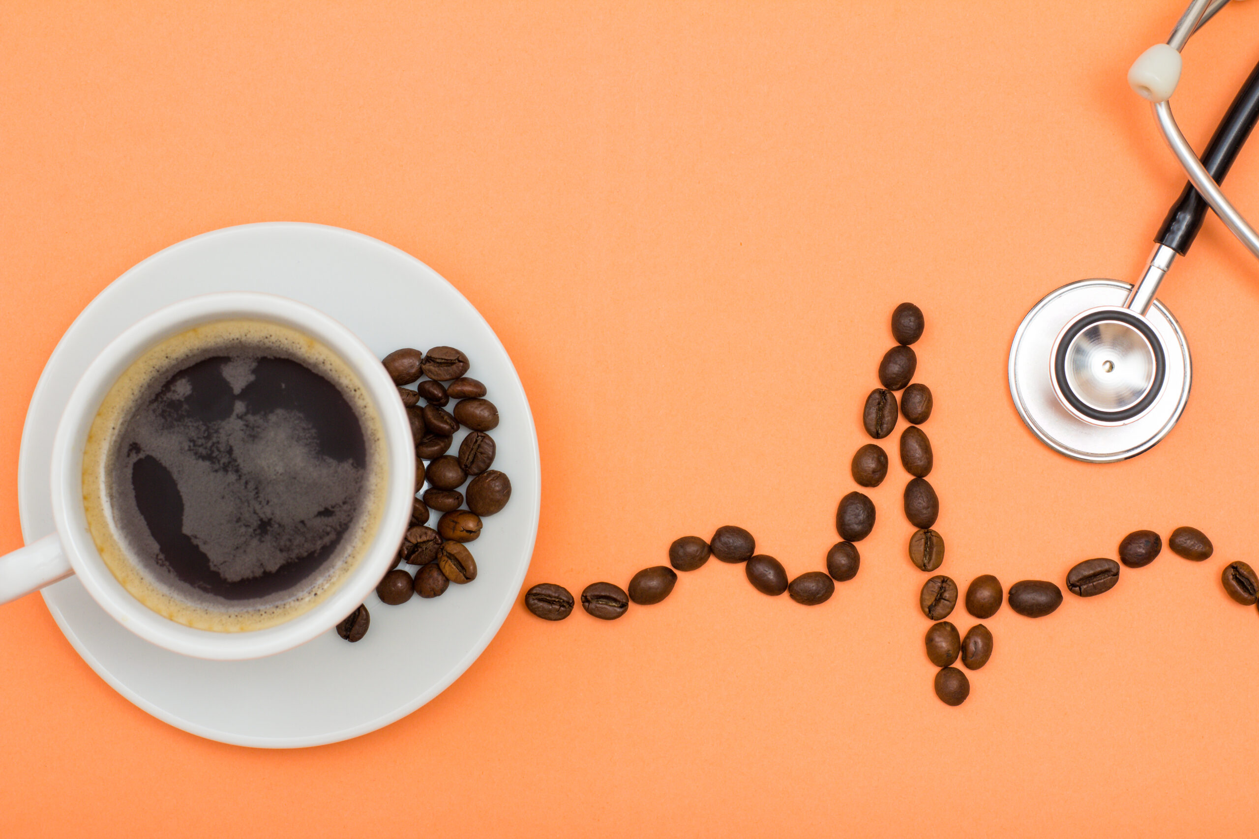 Image Cup of coffee on saucer with coffee beans folded in the form of a cardiogram and phonendoscope on peach colored background